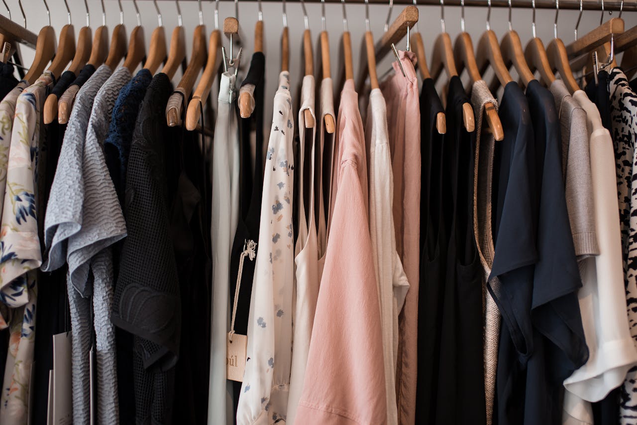 A stylish collection of women's clothing hanging on wooden hangers in a boutique setting.